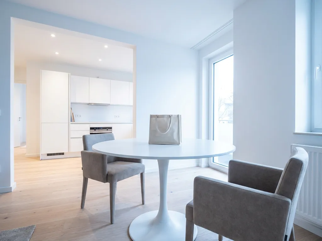 Minimalistisches Hannoveraner Apartment mit rundem weißem Tulpen-Esstisch, zwei greigefarbenen Stühlen und einer Stofftasche auf der Tischplatte.