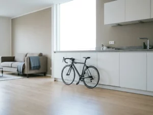 Fahrrad lehnt an weißen Küchenschränken in minimalistischer Hannoveraner Wohnung mit hellem Parkettboden und grauer Arbeitsplatte.