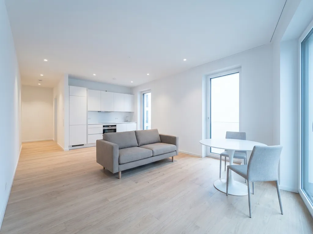 Minimalistisches Wohnzimmer in Hannover mit hellem Parkettboden, greigem Zweisitzer-Sofa und rundem weißem Tulpen-Esstisch.