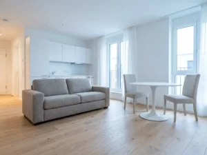 Helles Hannoveraner Apartment mit Parkettboden, greigem Zweisitzer-Sofa und rundem weißem Tulip-Esstisch vor offener Küche.