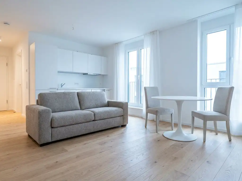 Helles Hannoveraner Apartment mit Parkettboden, greigem Zweisitzer-Sofa und rundem weißem Tulip-Esstisch vor offener Küche.