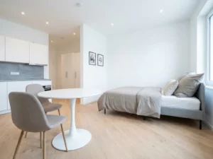 Minimalistisches Ein-Zimmer-Apartment in Hannover mit greigem Bett, Tulpen-Esstisch und hellem Holzboden.