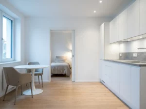 Minimalistisches Hannoveraner Apartment mit hellem Parkettboden, weißer Einbauküche, grauer Arbeitsplatte und rundem Tulpen-Esstisch.