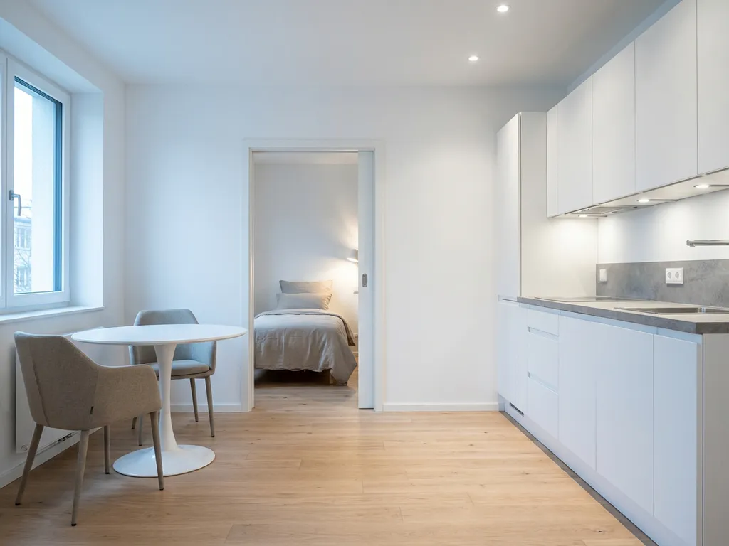 Minimalistisches Hannoveraner Apartment mit hellem Parkettboden, weißer Einbauküche, grauer Arbeitsplatte und rundem Tulpen-Esstisch.