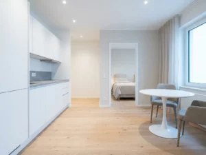Minimalistisches Hannoveraner Apartment mit hellem Parkettboden, weißer Einbauküche, grauer Arbeitsplatte und rundem Tulip-Esstisch.