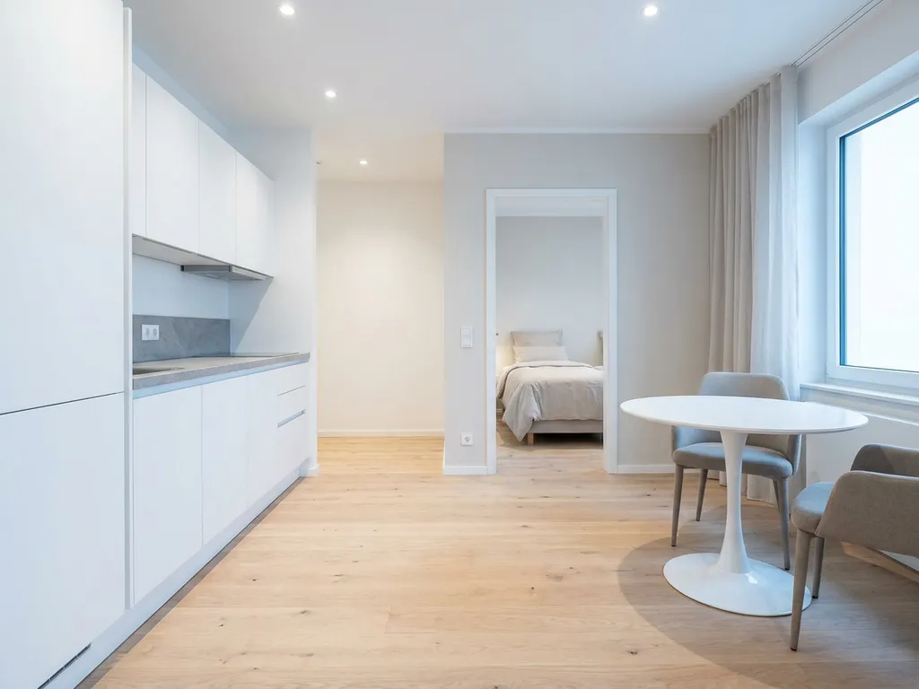 Minimalistisches Hannoveraner Apartment mit hellem Parkettboden, weißer Einbauküche, grauer Arbeitsplatte und rundem Tulip-Esstisch.