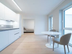 Leere, bezugsfertige Wohnung in Hannover mit hellem Parkettboden, weißer Einbauküche, grauer Arbeitsplatte und rundem Tulpen-Esstisch.
