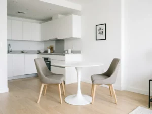 Minimalistisches Apartment mit rundem weißem Tulpen-Esstisch, greige Polsterstühlen und weißer Einbauküche auf hellem Eichenparkett.