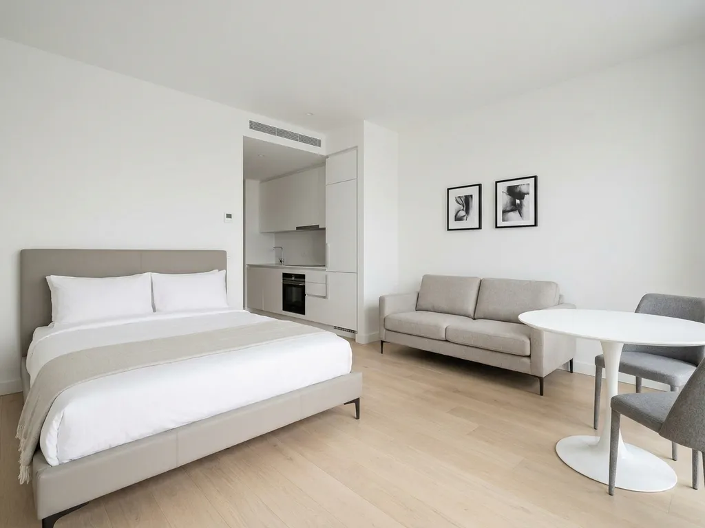 Minimalistisch eingerichtetes Apartment mit greigem Bett, weißer Küche, Tulpen-Esstisch und hellem Eichenholzboden.