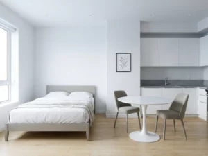 Minimalistisch eingerichtetes Apartment mit graubeigem Bettgestell, rundem Tulpen-Esstisch und hellem Eichenparkett.