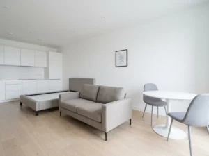 Minimalistisch eingerichtete Wohnung mit greigefarbenem Bett, weißem Tulpen-Esstisch und hellem Eichenparkett.