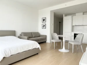 Minimalistisch eingerichtetes Apartment mit greigem Bett, Sofa, rundem Tulpen-Esstisch und hellem Eichenparkett.