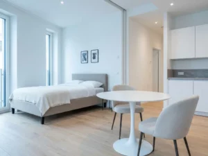 Minimalistisch eingerichtetes Apartment mit greigem Bettgestell, rundem Tulpen-Esstisch und hellem Eichenparkett.