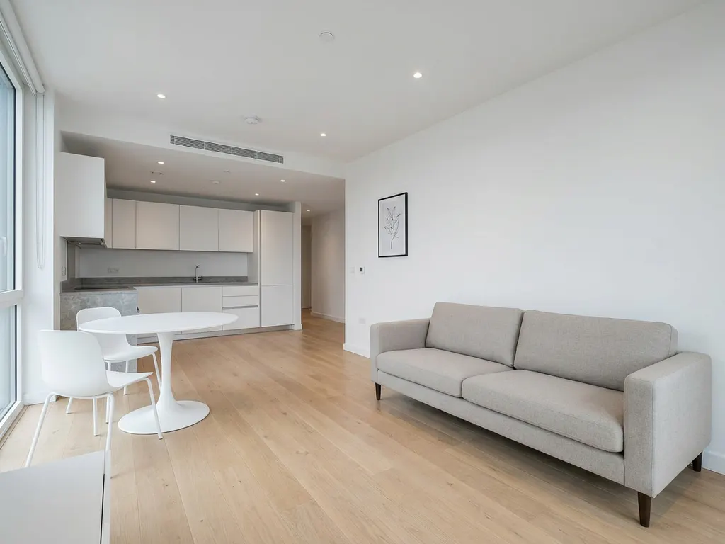 Minimalistisch eingerichtete Wohnung mit greigem Sofa, rundem Tulpen-Esstisch und hellem Parkettboden, weiße Küche im Hintergrund.