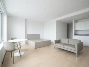 Minimalistisch eingerichtete Wohnung mit greigem Bett, weißem Tulpen-Esstisch und hellen Holzböden.