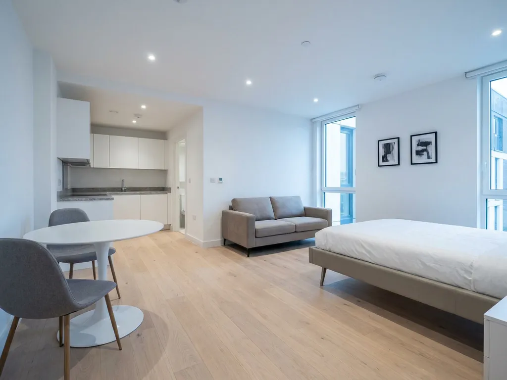 Minimalistisch eingerichtete offene Wohnung mit greigebeigem Sofa, Tulip-Esstisch, weißen Küchenfronten und hellem Eichenparkett.