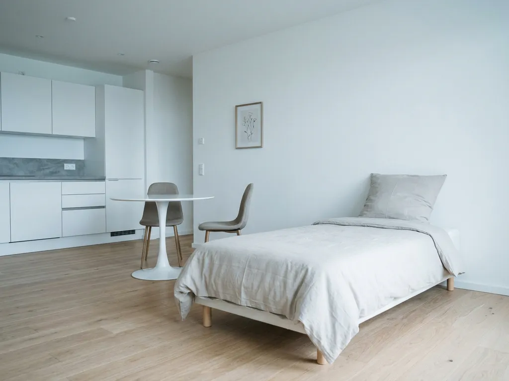 Minimalistisch möbliertes Apartment in Hannover mit hellem Holzboden, weißer Küche und rundem Tulpen-Esstisch.