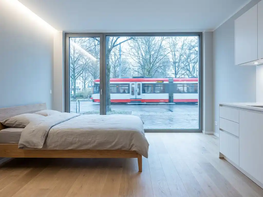 Minimalistisch eingerichtetes Apartment in Hannover mit hellem Parkettboden, weißer Küche und Stadtbahn im Hintergrund.