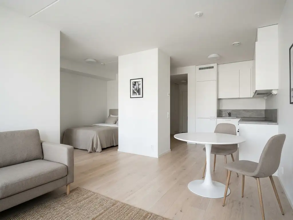 Minimalistisch eingerichtete Wohnung mit hellem Parkettboden, weißer Küche, rundem Tulpen-Esstisch und graubeigem Sofa in neutraler Farbpalette.