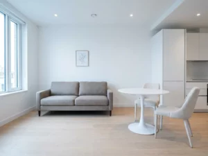 Minimalistisch eingerichtete Wohnung mit hellem Parkettboden, greigem Zweisitzer-Sofa und rundem weißem Tulip-Esstisch.
