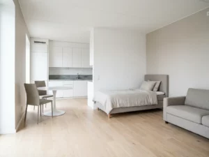 Minimalistisch eingerichtetes Apartment mit hellem Eichenparkett, weißer Tulpen-Esstisch, greige Polsterstühlen und Zweisitzer-Sofa.