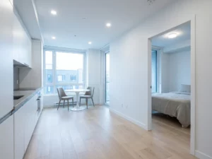 Minimalistisch eingerichtete Wohnung mit hellem Parkettboden, weißer Einbauküche, grauer Arbeitsplatte und rundem Tulpen-Esstisch.