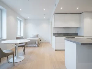 Minimalistisch eingerichtete Wohnung mit hellem Parkettboden, weißer Einbauküche, grauer Arbeitsplatte und rundem Tulpen-Esstisch.