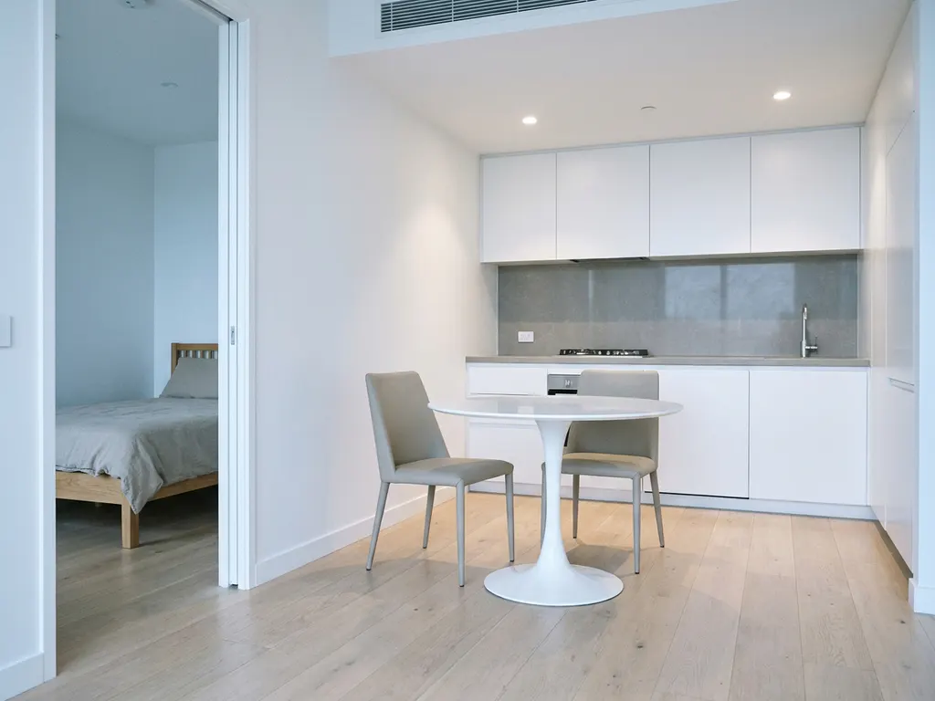 Minimalistisch eingerichtete Wohnung mit hellem Holzboden, weißer Küche, grauer Arbeitsplatte und rundem Tulpen-Esstisch mit zwei greigen Stühlen.