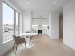 Minimalistisches Apartment mit rundem weißem Tulip-Tisch, greige Stühlen und Parkettboden, Blick durch helles Fenster auf Stadtstraße.