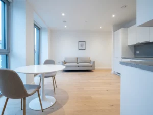 Minimalistisches Apartment mit rundem weißem Tulip-Esstisch, Greige-Stühlen, hellem Holzboden und offener Küche mit weißen Fronten.