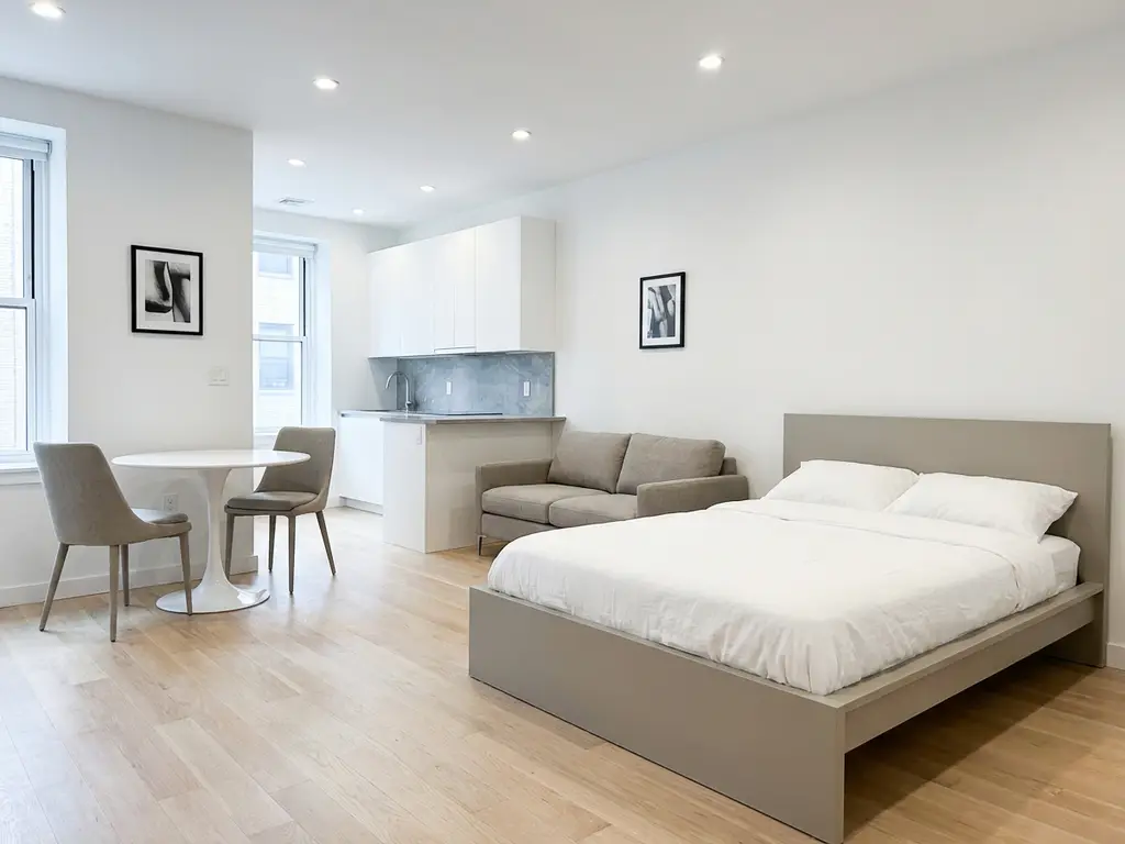 Minimalistisch eingerichtetes Apartment mit greigem Bettgestell, Zweisitzer-Sofa, rundem Tulpentisch und hellem Parkettboden.