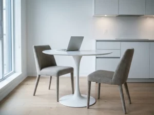 Aufgeklapptes Laptop auf rundem Tulpentisch in minimalistischer Wohnung mit hellem Holzboden und weißen Küchenfronten.