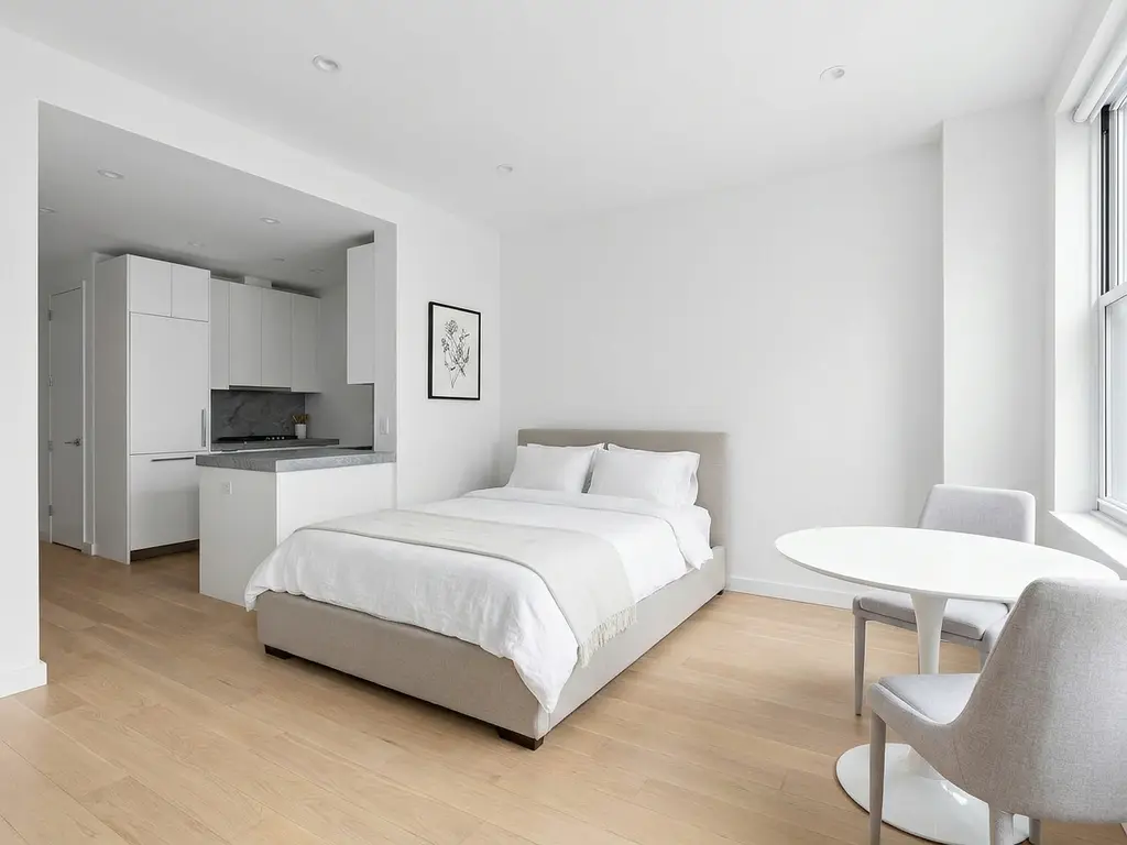 Minimalistisch eingerichtetes Apartment mit greigem Bettgestell, rundem Tulpen-Esstisch und hellem Eichenholzboden.