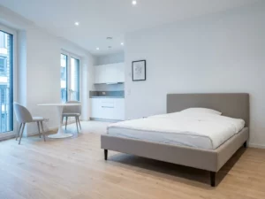 Minimalistisch möbliertes Apartment in Hannover mit greigem Bettgestell, rundem Tulpen-Esstisch und hellem Eichenparkett.