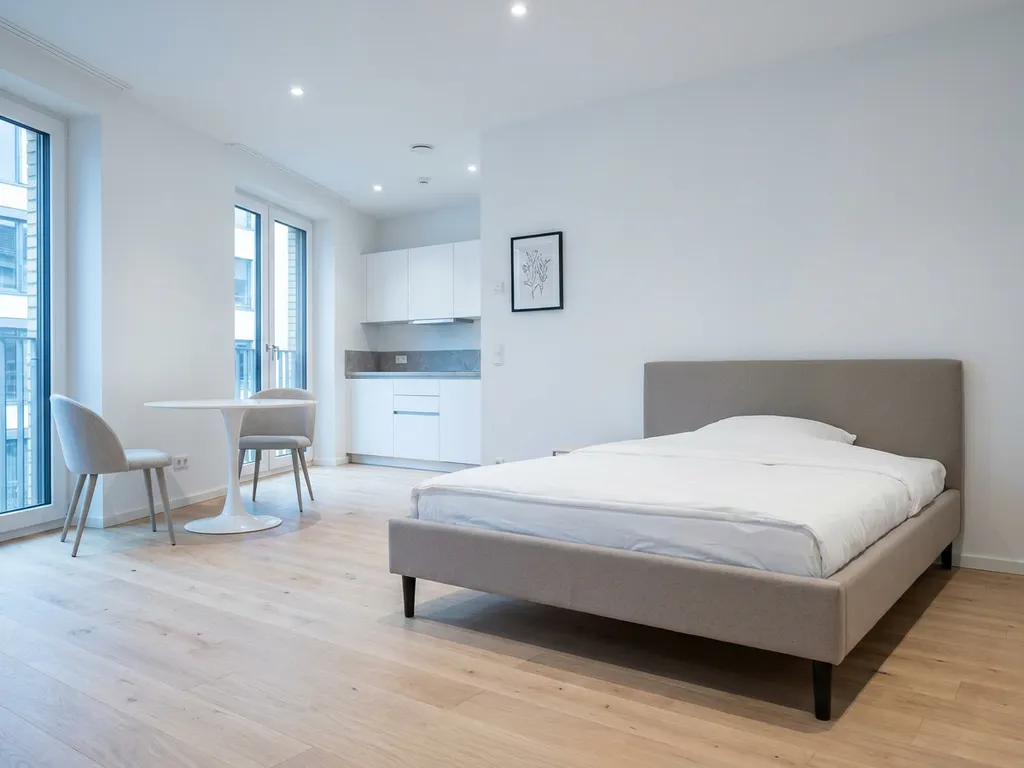 Minimalistisch möbliertes Apartment in Hannover mit greigem Bettgestell, rundem Tulpen-Esstisch und hellem Eichenparkett.