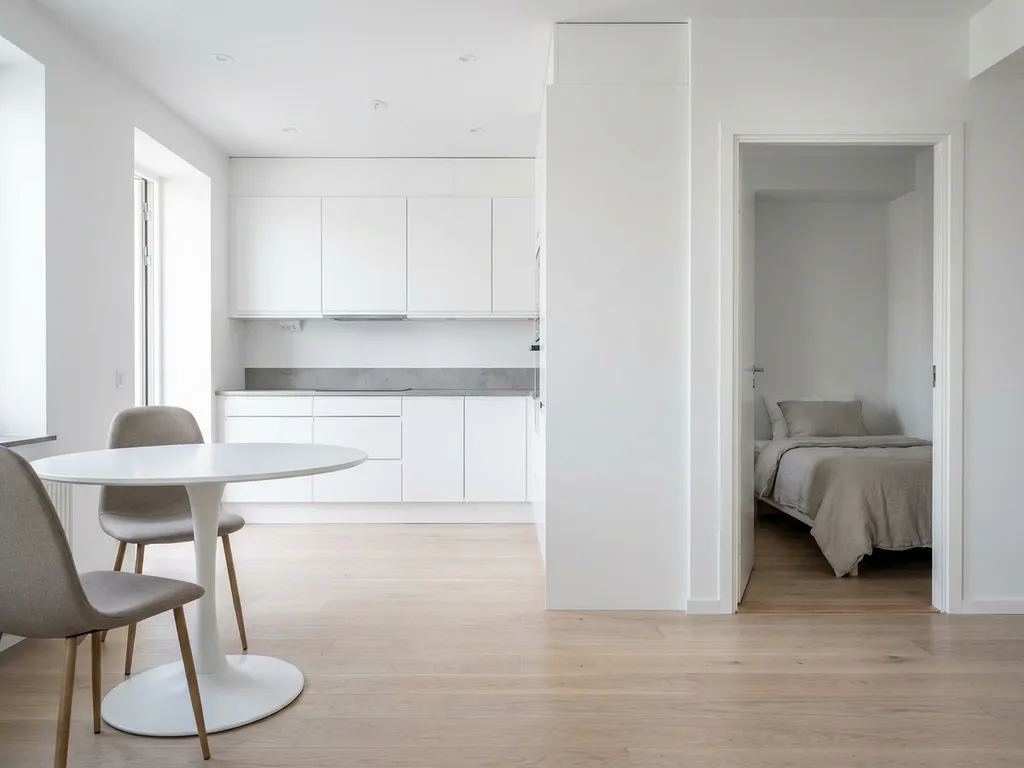 Minimalistisch eingerichtete Wohnung mit hellem Parkettboden, weißer Einbauküche, grauer Arbeitsplatte und rundem Tulpen-Esstisch mit greigen Polsterstühlen.