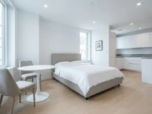 Minimalistisch eingerichtetes Apartment mit greigem Bettgestell, rundem Tulpen-Esstisch und hellem Eichenholzboden.