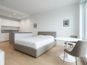 Minimalistisch eingerichtetes Apartment mit greigem Bettgestell, rundem Tulpen-Esstisch und hellem Eichenholzboden.