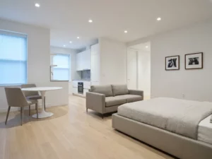 Minimalistisch eingerichtetes Studio-Apartment mit Greige-Bett, weißer Tulpen-Esstisch und hellen Eichenholzböden.