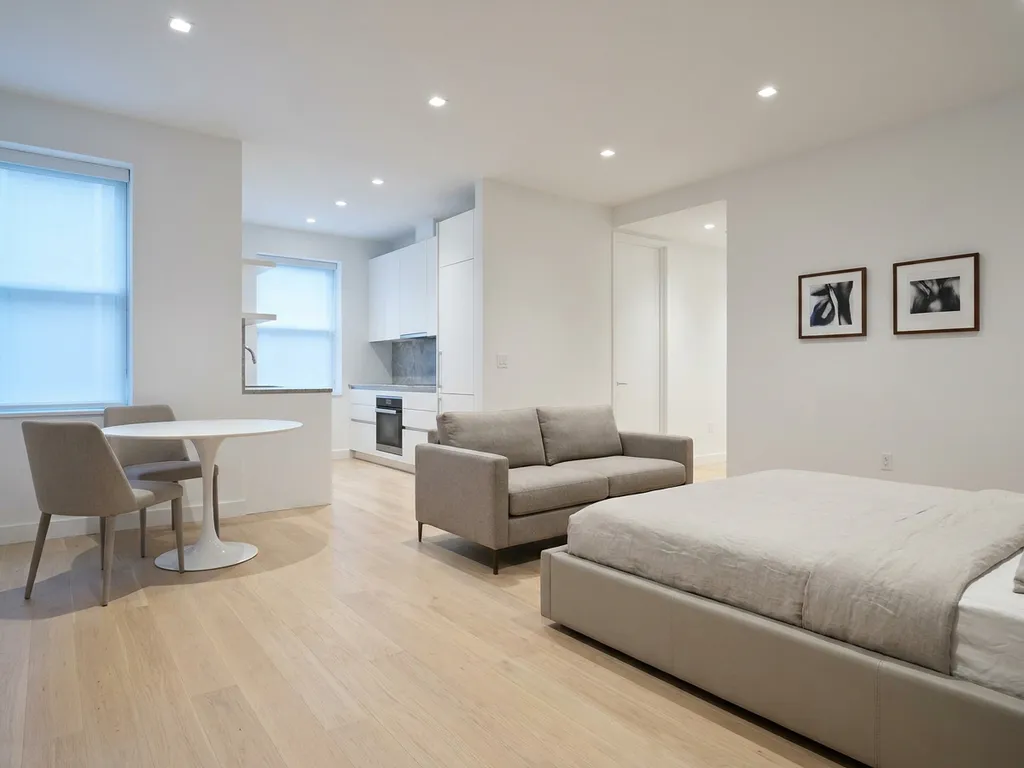 Minimalistisch eingerichtetes Studio-Apartment mit Greige-Bett, weißer Tulpen-Esstisch und hellen Eichenholzböden.