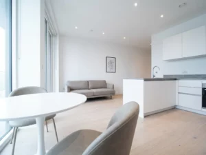 Minimalistisch möblierte Wohnung bei Übergabe mit rundem weißen Tulpen-Esstisch, greigen Polsterstühlen und hellem Eichenparkett.