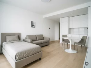 Minimalistisch eingerichtetes Apartment mit greigem Bett, weißer Tulpen-Esstisch, Zweisitzer-Sofa und hellen Holzböden.