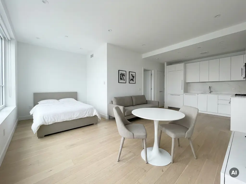 Minimalistisch eingerichtete Wohnung mit greigem Bett, Zweisitzer-Sofa, rundem Tulpen-Esstisch und weißer Küche im Hintergrund.