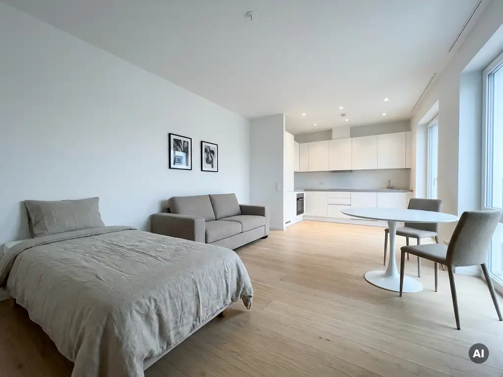 Minimalistisch eingerichtetes Apartment mit greigem Einzelbett, Zweisitzer-Sofa, rundem Tulpen-Esstisch und hellem Parkettboden.