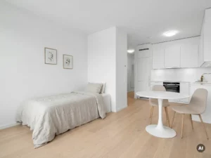 Minimalistisch eingerichtetes Apartment mit Einzelbett, rundem Tulpen-Esstisch und weißer Einbauküche auf hellem Parkettboden.